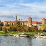 Kraków, miasto nad Wisłą, z Wawelem w jesiennej odsłonie. Statki wycieczkowe cumują przy brzegu.