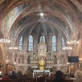 Wnętrze sanktuarium w Gietrzwałdzie, z ołtarzem głównym, witrażami i wiernymi na ławkach.