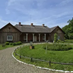 Drewniany dworek w skansenie Sanok, otoczony zielenią i kamienistą ścieżką, zaprasza do podróży w przeszłość.