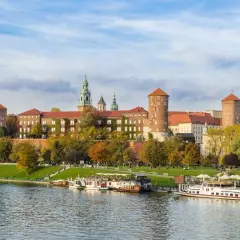 Kraków, miasto nad Wisłą, z Wawelem w jesiennej odsłonie. Statki wycieczkowe cumują przy brzegu.