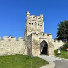 Kamienna brama z wieżą i murami obronnymi, jak z polskiego Carcassonne, w słoneczny dzień.