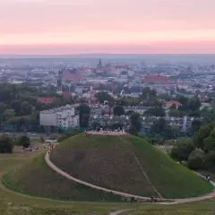 Zachód słońca nad Krakowem, z Kopcem Kraka na pierwszym planie, gdzie spacerują ludzie.