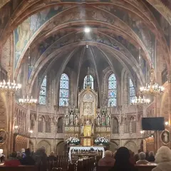 Wnętrze sanktuarium w Gietrzwałdzie, z ołtarzem głównym, witrażami i wiernymi na ławkach.