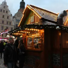 Tłumy ludzi na największym jarmarku bożonarodzeniowym w Polsce. Drewniana chatka ozdobiona lampkami i bombkami.