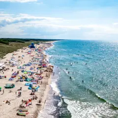 Plaża w Darłowie z turystami, parasolami i namiotami, w tle morze i las.