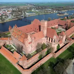 Potężny zamek w Malborku, jedna z największych atrakcji Polski, widziany z lotu ptaka. Rozległy kompleks z czerwonej cegły otoczony murami obronnymi, nad rzeką Nogat.