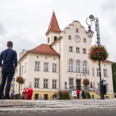Mężczyzna podziwia ratusz w Trzebnicy, jedną z głównych atrakcji miasta. W tle czerwone serce i kwitnące kwiaty.
