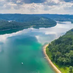 Malownicze jezioro otoczone lasami, z żaglówkami przy brzegu. To jedne z wielu pięknych walorów turystycznych Polski, idealne miejsce na wypoczynek.