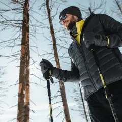 Mężczyzna w zimowej kurtce i czapce z nartami w rękach, w lesie. Czy to firma Viking? Tak, to sprzęt Viking.