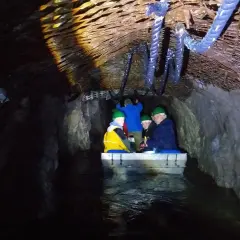 Podziemna łódź z turystami w kaskach płynie przez tunel. Czy to osówka czy włodarz, trudno stwierdzić w mroku.