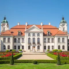Pałac Zamoyskich w Kozłówce, z czerwonym dachem i wieżyczkami, otoczony kwitnącym ogrodem z czerwonymi różami.