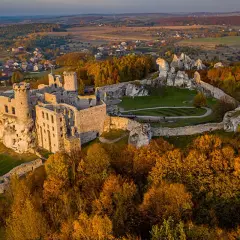Zamek Ogrodzieniec w jesiennej szacie, majestatycznie wznoszący się wśród skał i kolorowych drzew.
