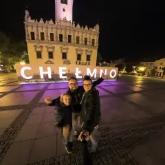Rodzina pozuje do zdjęcia na tle napisu "Chełmno" i ratusza nocą.