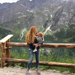 Kobieta z dzieckiem na rękach podziwia malowniczy widok Tatr. Wspaniałe **Zakopane z wózkiem** to idealne miejsce na rodzinne wycieczki.
