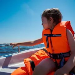 Dziewczynka w kamizelce ratunkowej cieszy się rejsową przygodą. To przykład bezpieczeństwa na wakacjach nad wodą.