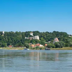 Widok na zamek i miasteczko na wzgórzu, z rzeką i łodziami na pierwszym planie. Kazimierz Dolny trasa zachwyca.
