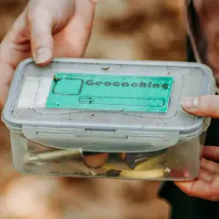 Pudełko z napisem "Geocaching" i drobiazgami w środku. To świetna zabawa, która polega na szukaniu ukrytych skarbów.