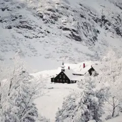 Zimowe Karkonosze otulone śniegiem. Domki z czerwonymi dachami ukryte wśród ośnieżonych drzew, na tle skalistych zboczy.
