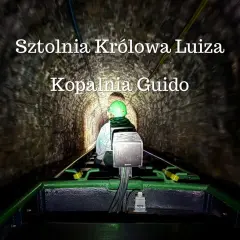 Osoba w kasku jedzie kolejką w ciemnej sztolni Królowa Luiza, Kopalnia Guido.