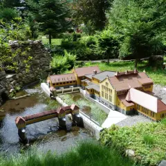 Miniaturowa zabudowa z mostkiem i rzeką, jak w parkach miniatur w Polsce.