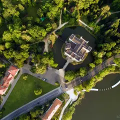 Zamek w Kórniku otoczony fosą i parkiem, widziany z lotu ptaka. Malowniczy krajobraz z drogą i budynkami w tle.