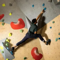 Wspinacz na ściance używa magnezji, by mieć pewniejszy chwyt. Widać kolorowe chwyty i czerwone "bouldery".