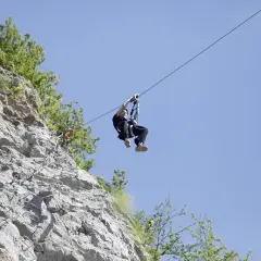 Człowiek zjeżdża na tyrolce obok skalnej ściany z ubezpieczeniami, jak na via ferrata polska.