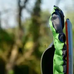 Zielona mata samopompująca z szarymi elementami, gotowa na biwak. Obok niej leży pomarańczowy materac.