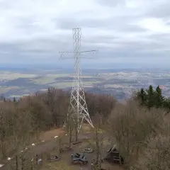Wielki metalowy krzyż góruje nad lasem na **chełmiec szczyt**. W oddali rozciąga się panorama miasta i pagórkowatego krajobrazu.