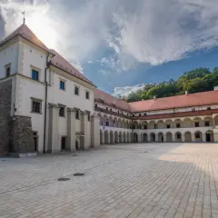 Zamek w Suchej Beskidzkiej z dziedzińcem i arkadowymi krużgankami. W tle zielone wzgórza.