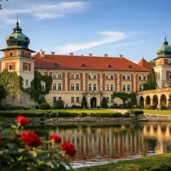 Pałac w Łańcucie, otoczony zielenią i kwitnącymi różami, z odbiciem w stawie. Wspaniałe łańcut atrakcje.