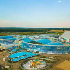 Największy aquapark w Polsce z błękitnymi, szklanymi dachami i kolorową fasadą, otoczony zielenią i basenami.