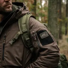 Mężczyzna w brązowej kurtce z naszywką Helikon-Tex, gotowy na przygodę. To dowód, że polskie marki outdoorowe to jakość i styl.