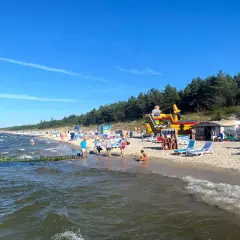Plaża w Grzybowie pełna życia: dmuchany zamek, leżaki i tłumy plażowiczów cieszących się słońcem.