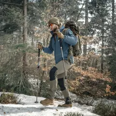 Mężczyzna z plecakiem i kije trekkingowe przemierza ośnieżony las.