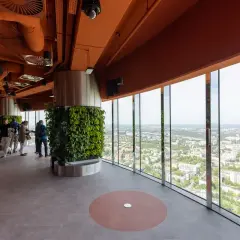 Wnętrze wieży widokowej we Wrocławiu z panoramicznym widokiem na miasto. Grupa ludzi zwiedza, podziwiając zieleń i architekturę.