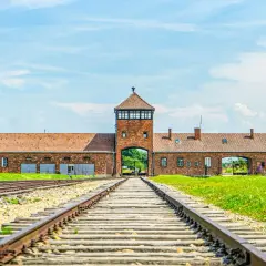 Brama obozowa w Oświęcimiu, z torami kolejowymi prowadzącymi do niej. Miejsce pamięci, które jest ważną częścią historii i atrakcją turystyczną.