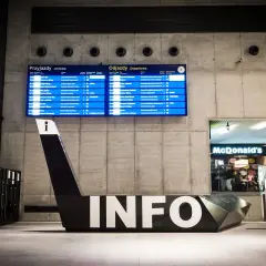 Nowoczesny dworzec w Katowicach. Tablice z odjazdami i przyjazdami, charakterystyczny napis INFO i McDonald's. Atrakcje dla podróżnych.
