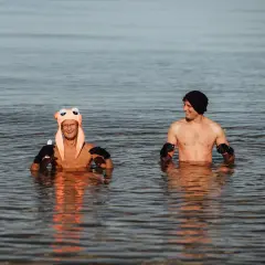 Dwóch mężczyzn w wodzie, jeden w zabawnej czapce, drugi w czarnej. Morsowanie w niskiej temperaturze wody.