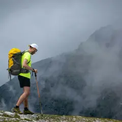 Mężczyzna z plecakiem i kijkami trekkingowymi wchodzi na mglisty szczyt. Wspaniały wyjazd w góry!