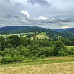 Zielone wzgórza i lasy w Węgierskiej Górce zapraszają na piesze wędrówki. Widok na dolinę i chmury na niebie.
