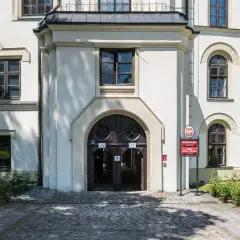 Wejście do zabytkowego zamku w Żywcu, z charakterystycznymi drzwiami i oknami. Obok tablica informująca o Muzeum Miejskim i Urzędzie Stanu Cywilnego.