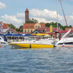 Żółta i białe łodzie motorowe cumują w porcie, w tle zabudowania i wieża. Idealne miejsce na bon Warmia Mazury.