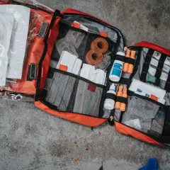 Rozłożona apteczka turystyczna z wyposażeniem: plastry, bandaże, płyn dezynfekujący, strzykawki.