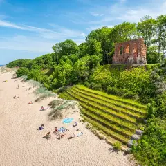 Piękna plaża z ruinami na wzgórzu, zielone zbocza i ludzie odpoczywający na piasku. Trzęsacz atrakcje zachwycają!