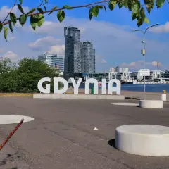 Napis GDYNIA na tle nowoczesnej architektury i żaglowca. Widok z Gdynia Rynek Główny.