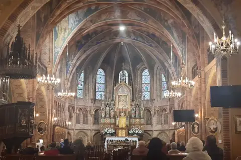 Wnętrze sanktuarium w Gietrzwałdzie, z ołtarzem głównym, witrażami i wiernymi na ławkach.