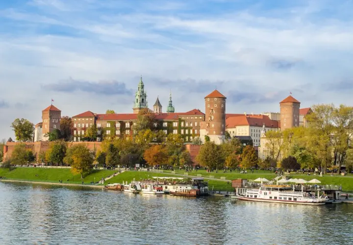 Kraków, miasto nad Wisłą, z Wawelem w jesiennej odsłonie. Statki wycieczkowe cumują przy brzegu.