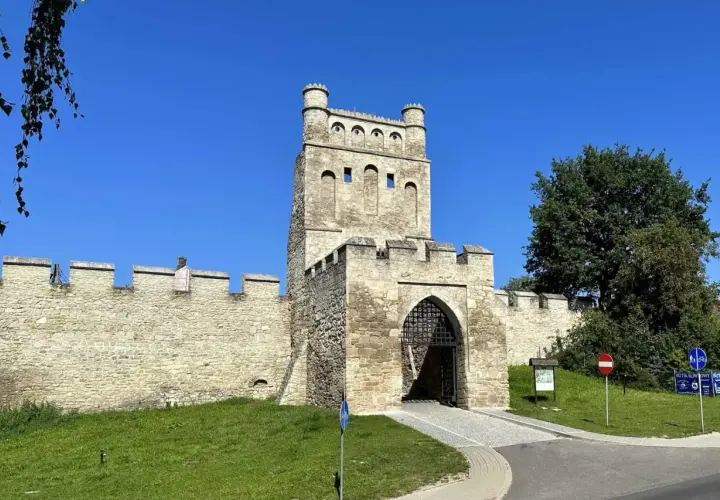 Kamienna brama z wieżą i murami obronnymi, jak z polskiego Carcassonne, w słoneczny dzień.