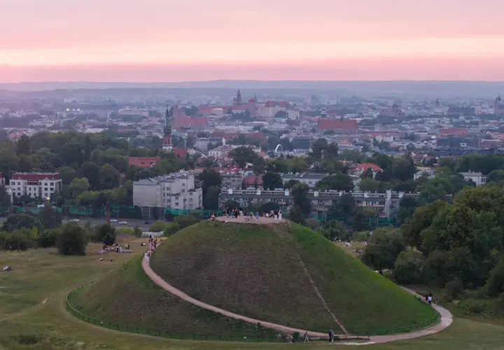 Zachód słońca nad Krakowem, z Kopcem Kraka na pierwszym planie, gdzie spacerują ludzie.